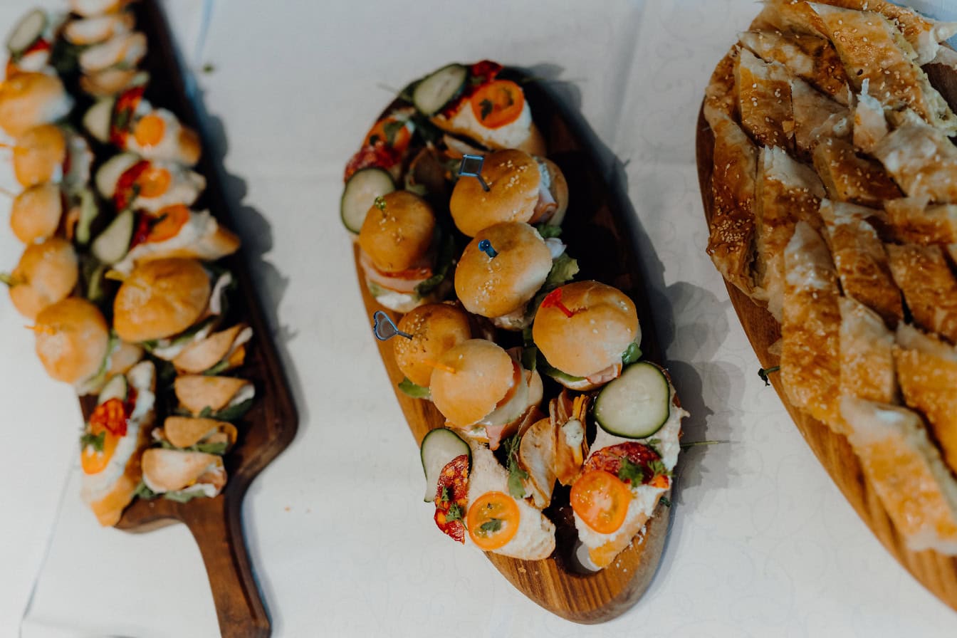 Wooden plates with small burgers and sandwiches, an appetizer food on table with white tablecloth