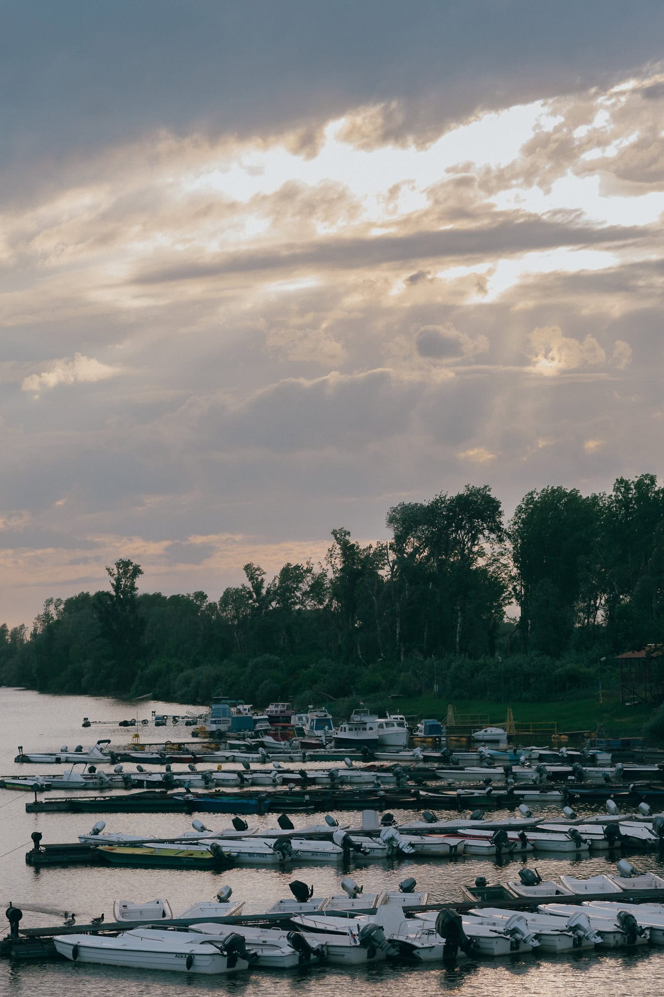 Small fishing boats in a lake harbor at dusk with sunrays through thick clouds