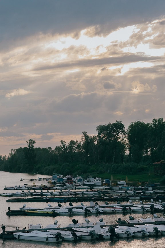 Bărci mici de pescuit într-un port de lac la amurg cu raze de soare printre nori groși