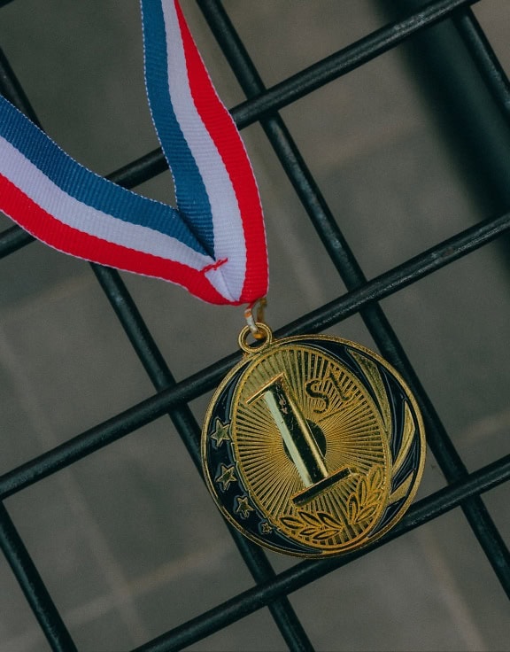 Una medalla de oro grabada con la inscripción 1ª, con cinta roja, blanca y azul sobre una rejilla de alambre negro