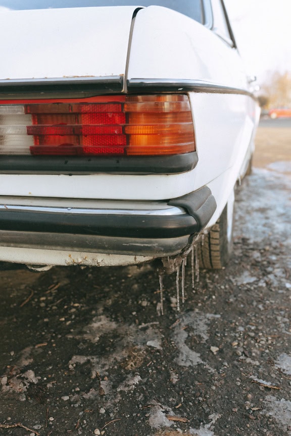 The rear end of the old-timer sedan with taillights and with icicles on the bumper