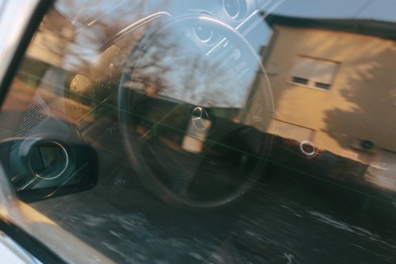 A photo through window of an interior of a car with a Mercedes Benz logo on a steering wheel