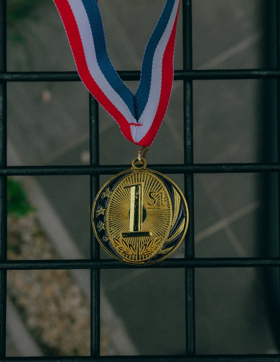 Goldmedaille mit einem roten, weißen und blauen Band, das an einem schwarzen Zaun hängt