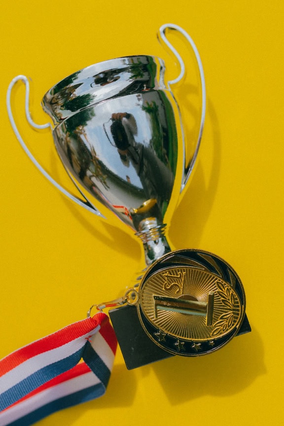 Silver trophy and a gold medal on it on a yellow background, a prize for wining competition