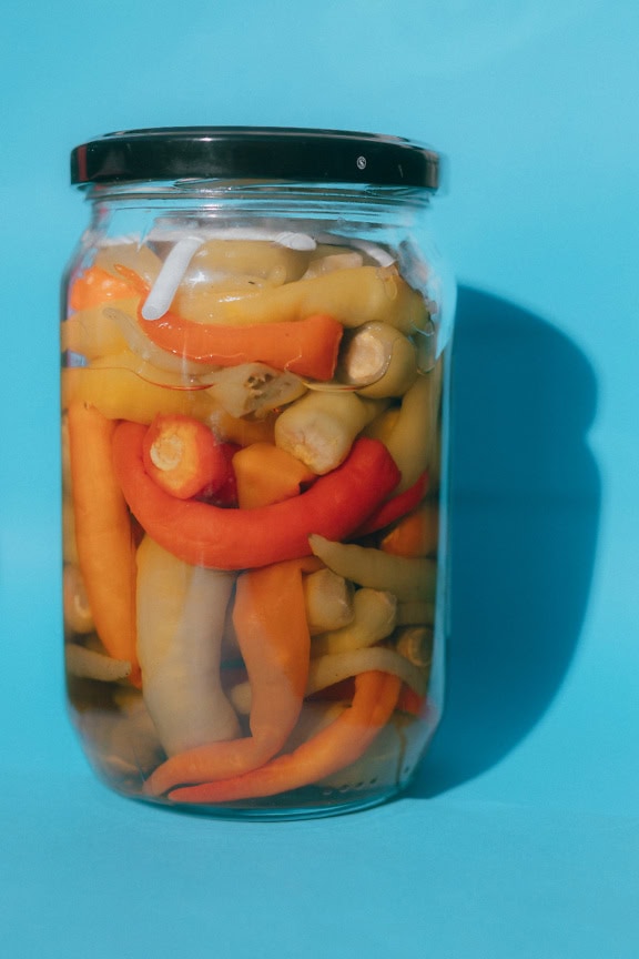 A jar with a homemade orange-yellow hot chili peppers on a blue background