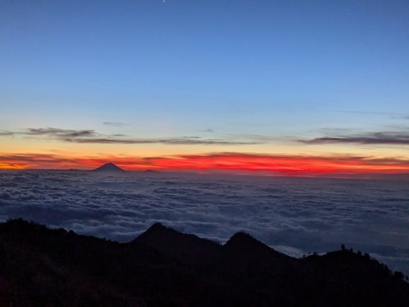 Panorama matahari terbenam dengan langit biru-merah di atas awan di gunung Rinjani di Indonesia