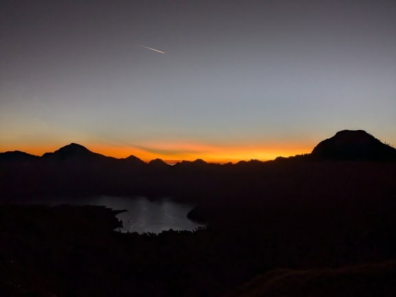 Apus de soare peste un lac cu o stea căzătoare pe cerul întunecat