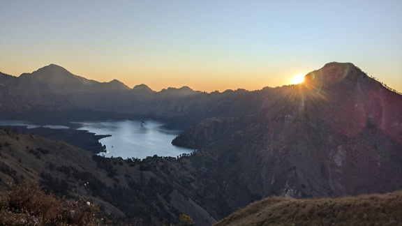 Słońce przebijające się przez chmury nad jeziorem kraterowym w kraterze wulkanicznym na górze Rinjani, aktywnym wulkanie na wyspie Lombok w Indonezji