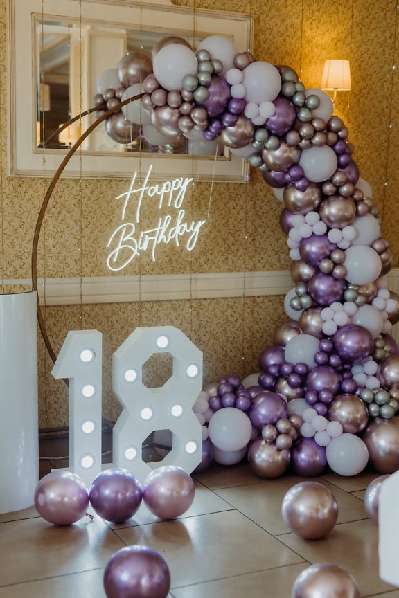 Balloon arch with glowing white neon sign Happy Birthday and the number eighteen (18), decoration to celebrate adulthood