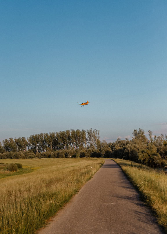 A biplane aircraft flying over a countryside road