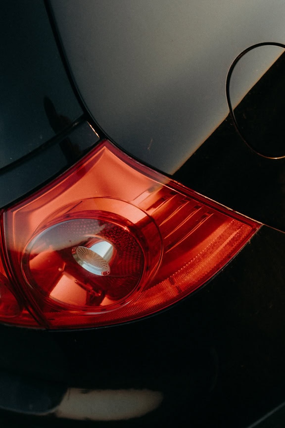 The back of a metallic black car with dark red rear light in the focus