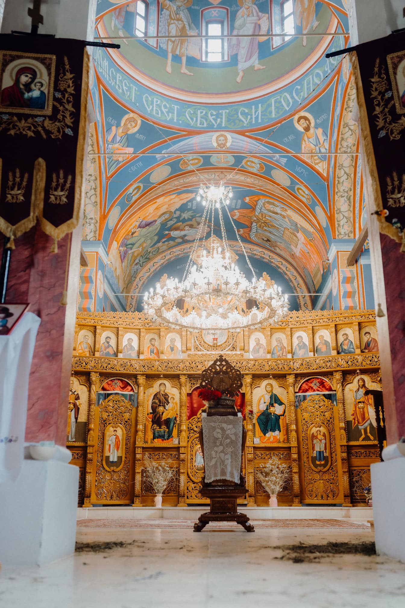 Majestätisch verzierter Altar mit Heiligenikonen in der orthodoxen Kirche mit einem großen leuchtenden Kronleuchter, der mit Mosaiken von der Decke hängt