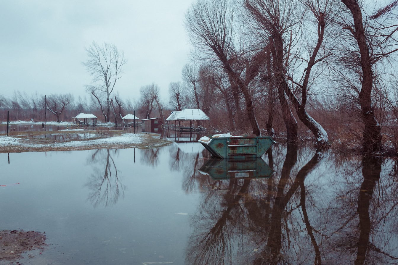 Landschaft eines überfluteten Parks mit einem Müllcontainer im Hochwasser an kaltem Winternachmittag