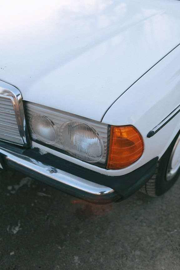 The front of a white Mercedes Benz sedan, an old-timer car with headlight in focus