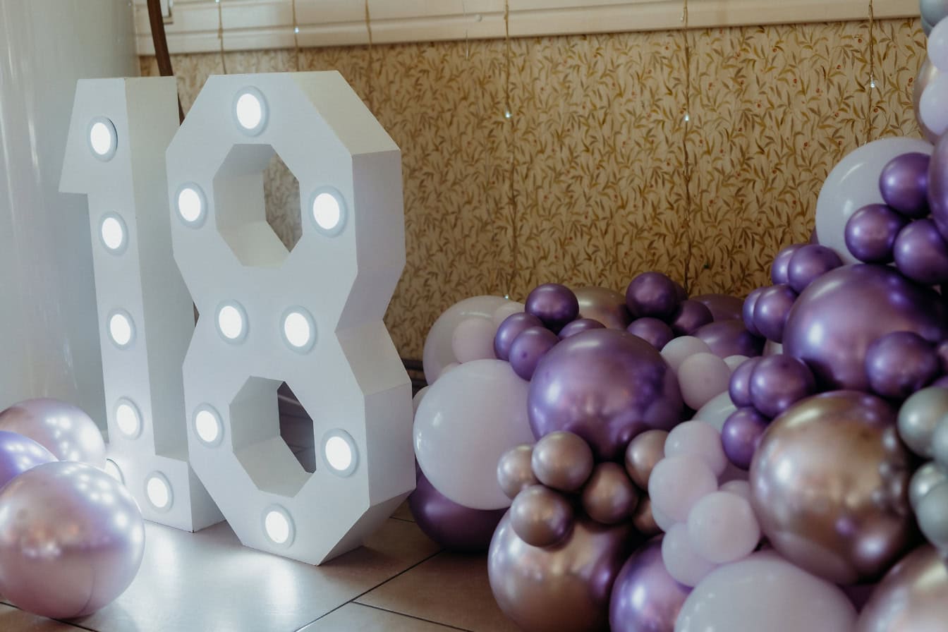 Decoração com luzes em forma de número dezoito (18) com balões roxos na festa de aniversário