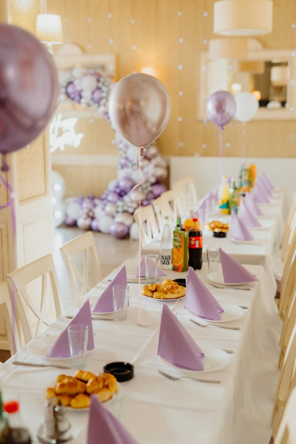 Feesttafel met borden en roze-paarse ballonnen en papieren servetten