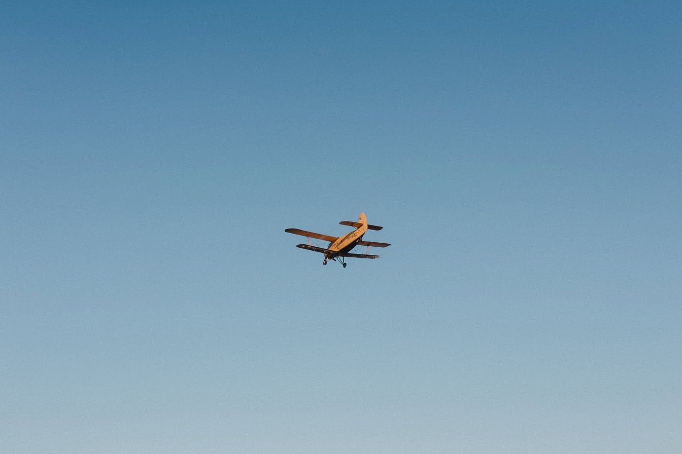 Et landbrugsfly, gammelt biplan-fly, der blev brugt til sprøjtning, flyver på den blå himmel