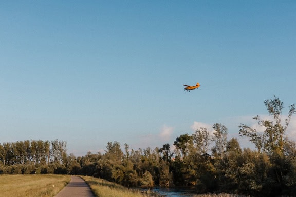 Biplan flyver over en asfaltsti og kanal på landet