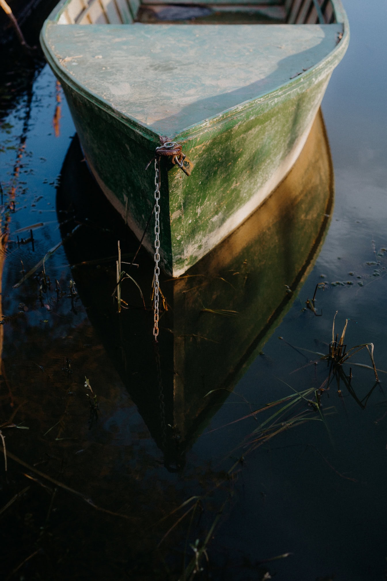 The bow of an old dark green river boat with a chain moored to the shore