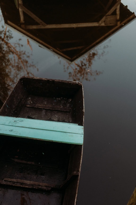 Wooden river boat on water with a reflection of boathouse