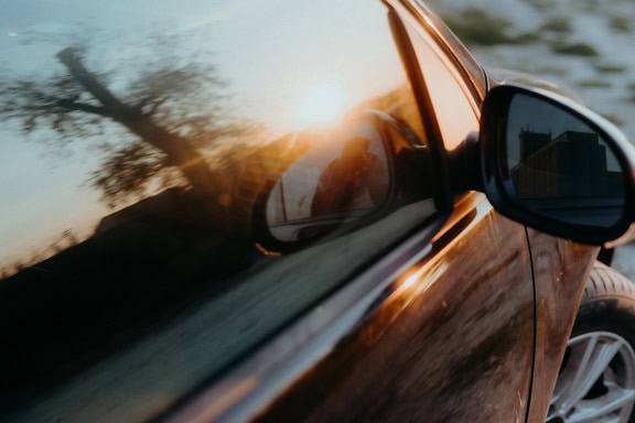 Ein Fotograf, der sich in einem Autospiegel spiegelt, mit hellen Sonnenstrahlen, die sich im Autofenster spiegeln