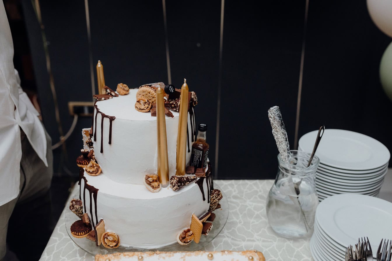 Gâteau d’anniversaire blanc avec des bougies dorées, des biscuits et du chocolat fondu dessus