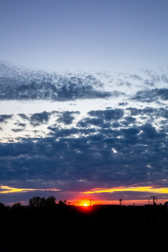 The color of the sky from light blue to dark blue to orange-yellow at sunset with the silhouette of the settlement