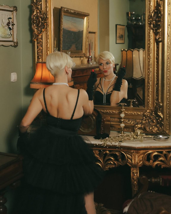 An attractive woman in an extravagant glamorous dress looking in the mirror while holding lipstick