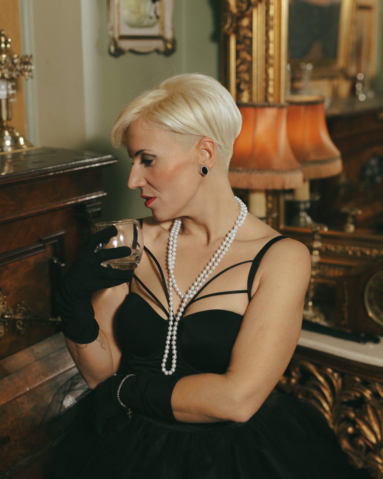 Portrait of an extravagant lady posing in a glamorous black dress and gloves while holding a glass