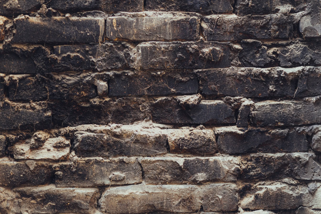 Texture d’un mur de briques avec des briques noires fuligineuses noircies par la fumée, maçonnerie par empilement horizontal de briques d’argile avec du ciment