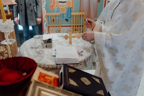 Ein orthodoxer Priester in weißem Gewand hält während der heiligen Liturgie ein goldenes Kreuz über der Bibel