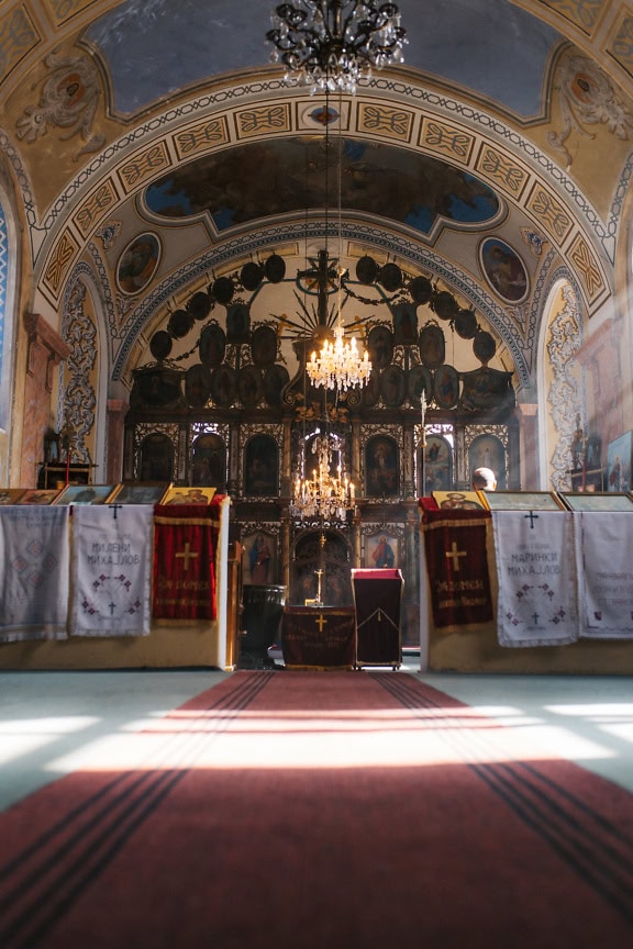 Fotografia sakralna wykonana pod niskim kątem wnętrza kościoła z żyrandolem i ołtarzem z ikonami w tle