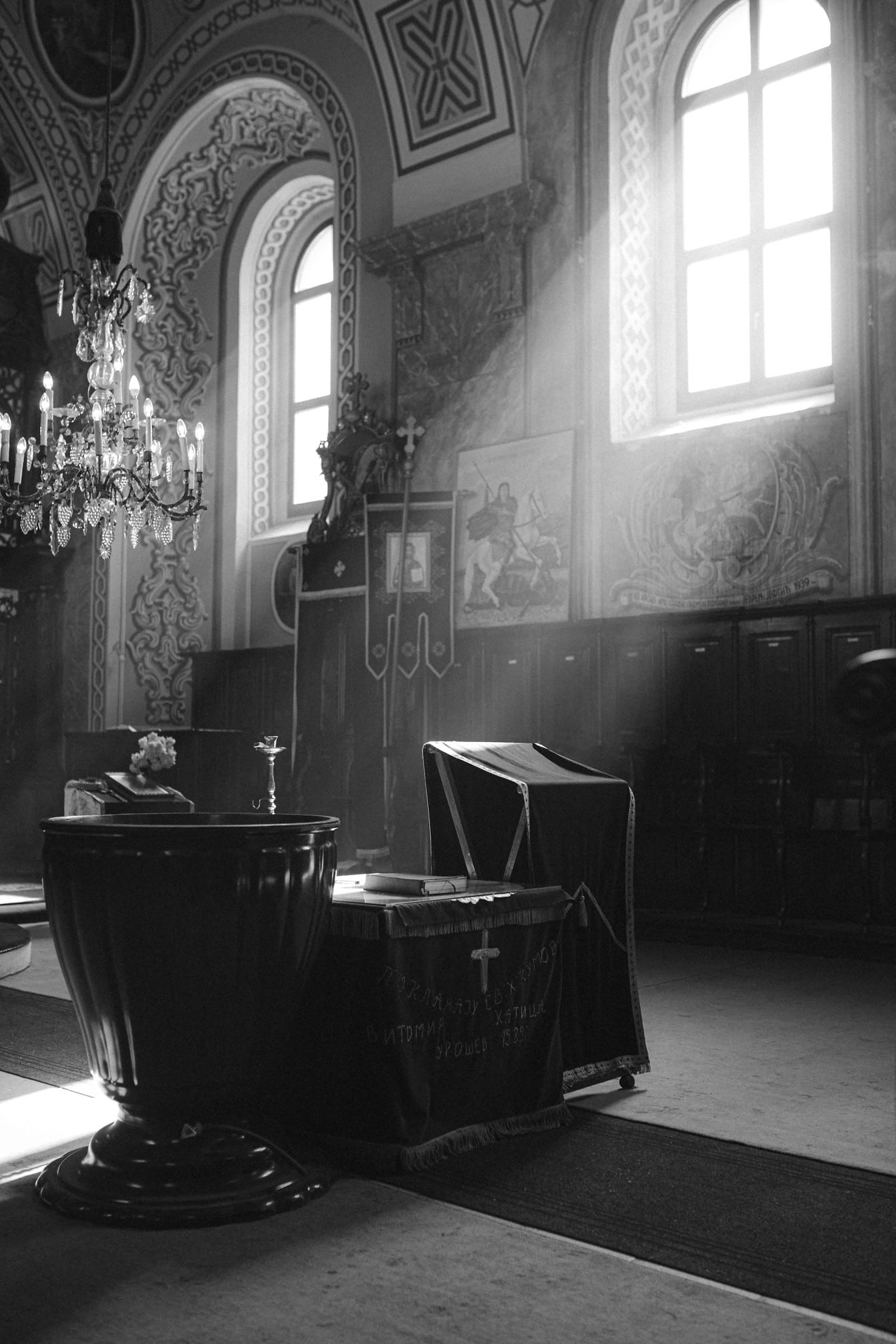 Photographie sacrée en noir et blanc illustrant la descente de l’Esprit Saint sur la table du baptême avec les rayons du soleil à travers la fenêtre