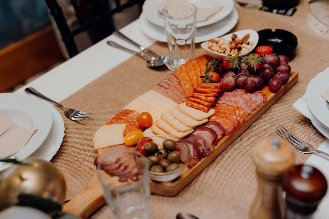 Schotel van varkensvlees en kaas met rode druiven en olijven op een ontbijttafel