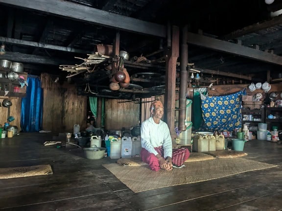 Mann som sitter på en matte i et tradisjonelt hjem i etnolandsby på Bali, Indonesia