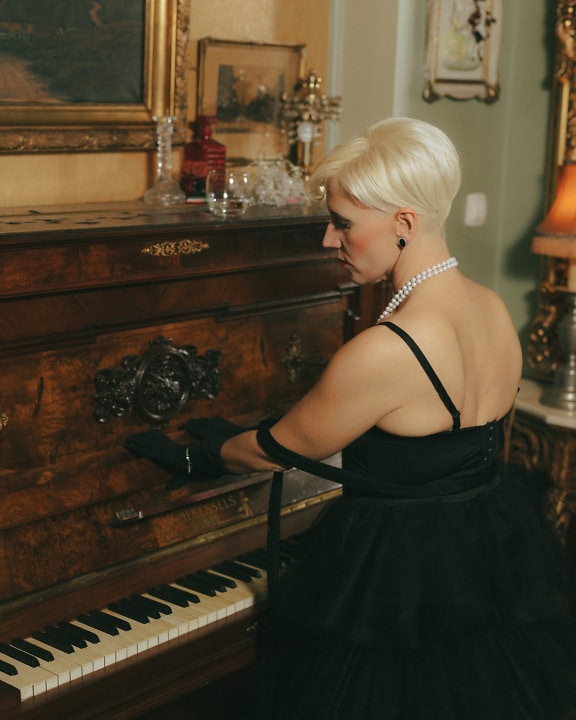 Une jolie pianiste se tient au piano, une femme en robe noire prête à jouer du piano