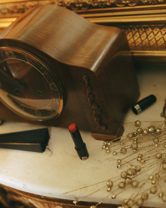 Une horloge en bois de style baroque antique et du rouge à lèvres rouge sur une table