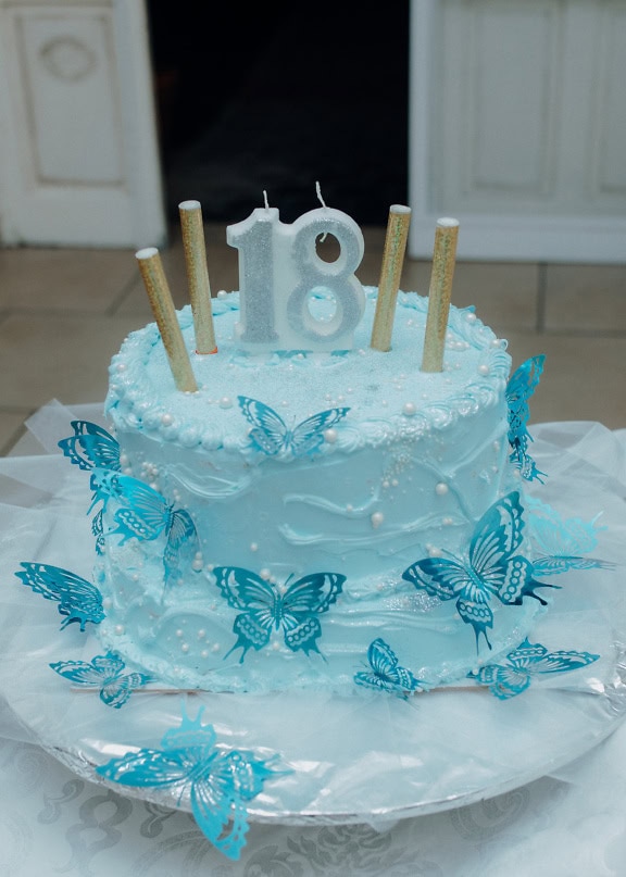 Torta di compleanno con una candelina con il numero diciotto (18) e una decorazione a forma di farfalle in cima