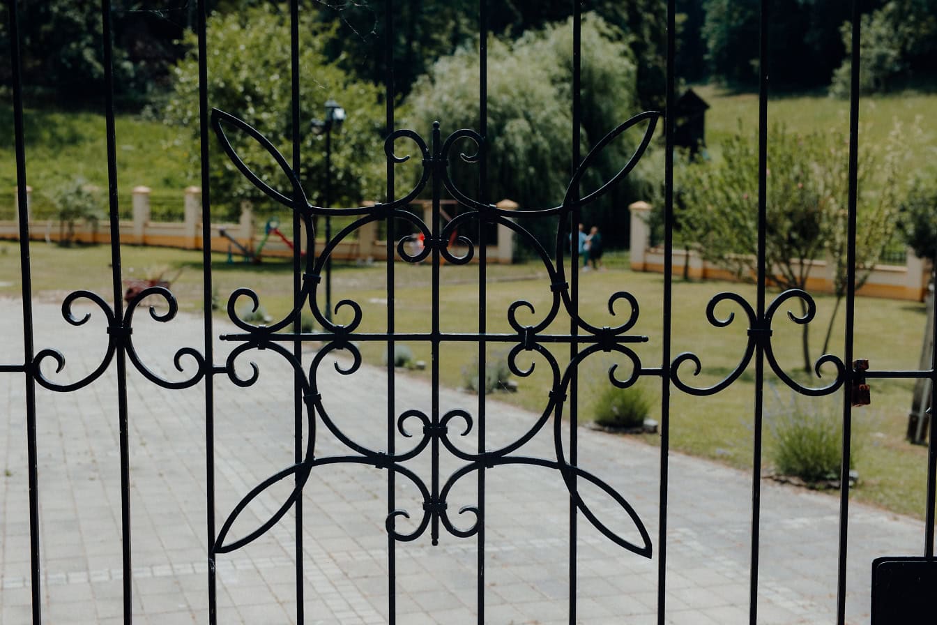 Cast iron gate with ornaments and with lawn in backyard in the background