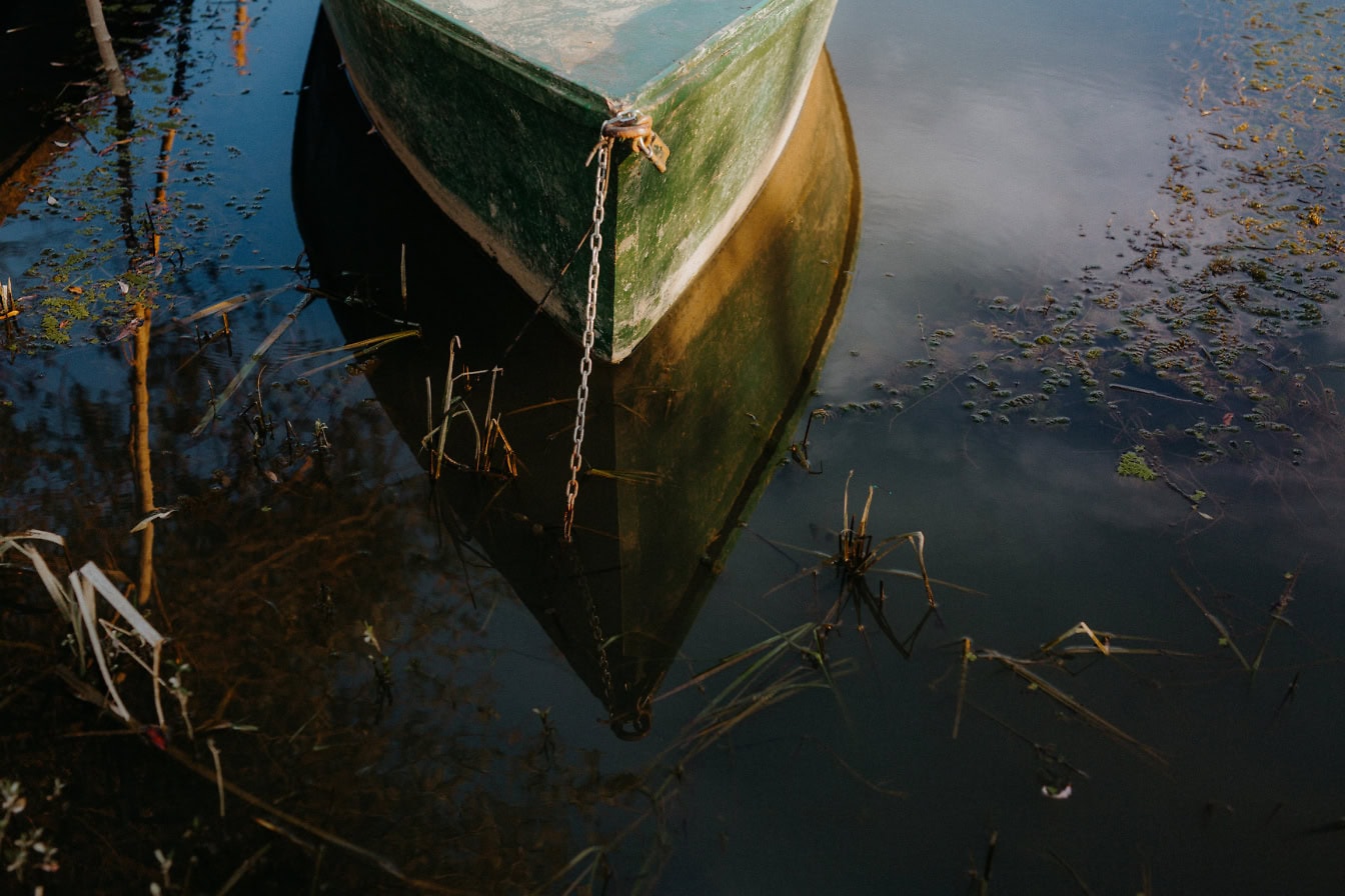 Barco de plástico verde oscuro amarrado con cadena en el agua