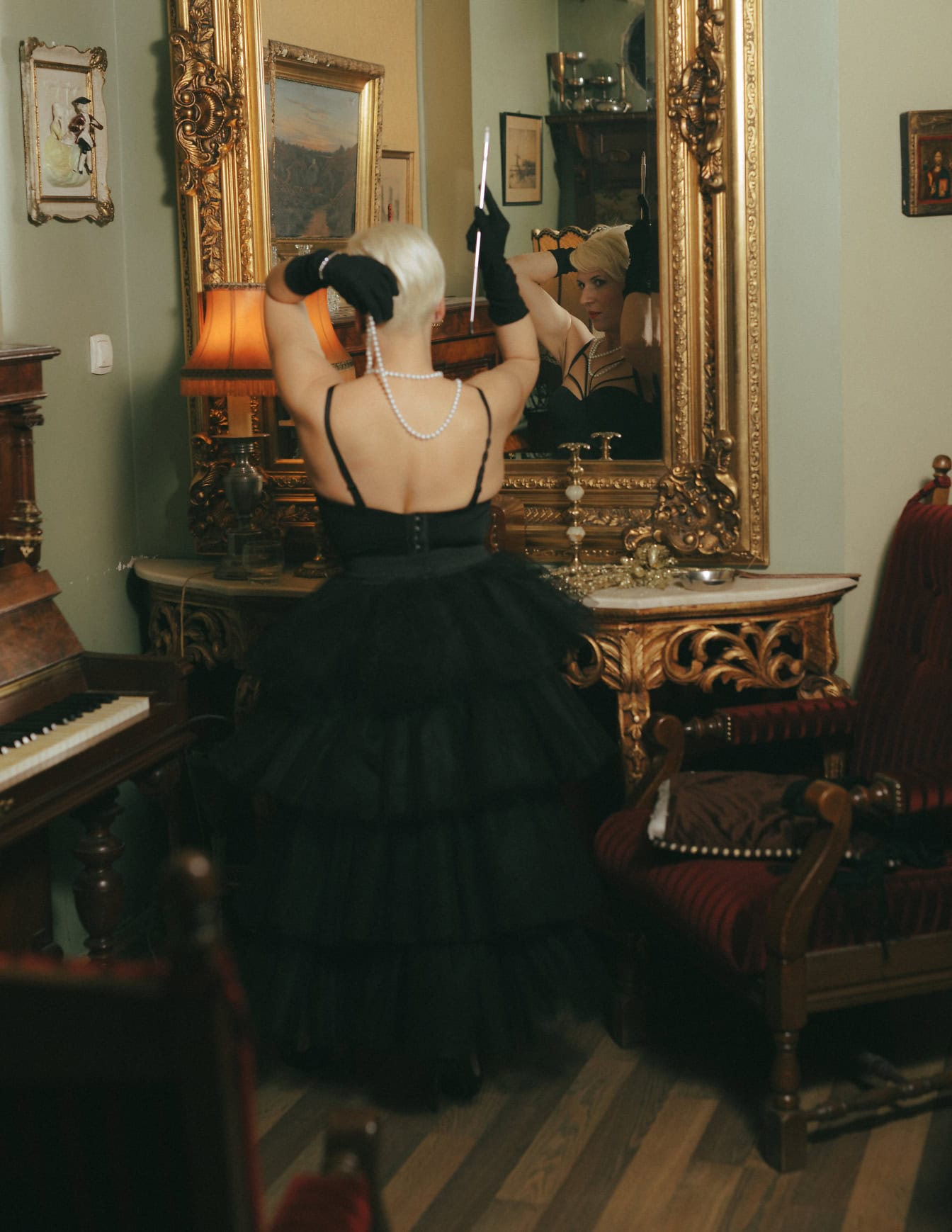 Mujer joven glamurosa en un vestido negro de moda posando frente al espejo en una habitación decorada de estilo barroco