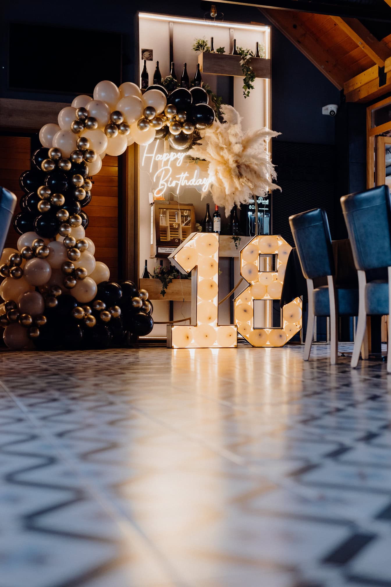 Arche de ballons avec néons Happy Birthday et le numéro 18 dans une cave rustique-moderne, un endroit parfait pour célébrer l’âge adulte