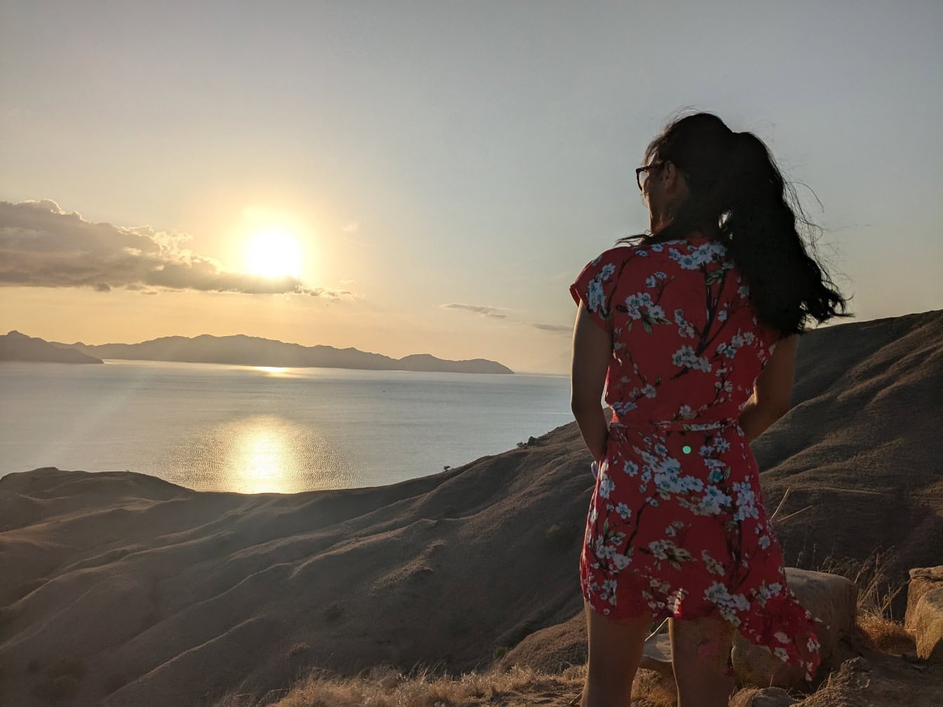 Woman in red dress standing on a hill looking at the sunset over bay