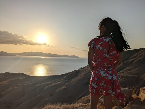 Woman in red dress standing on a hill looking at the sunset over bay