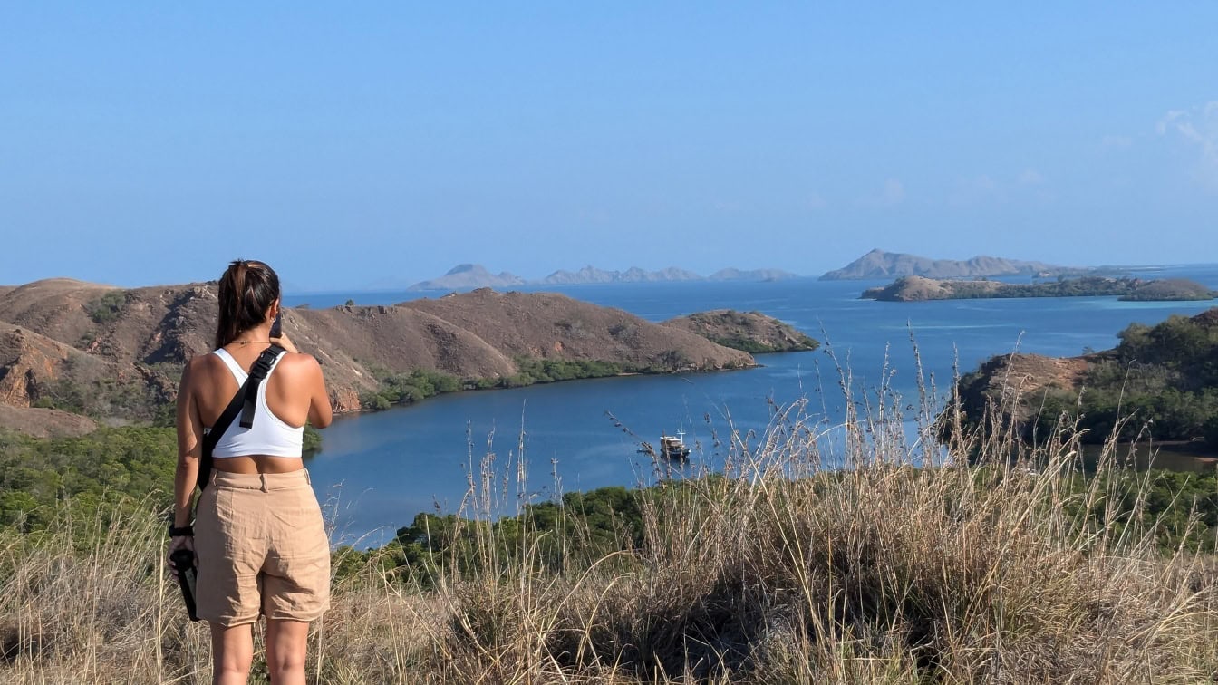 Mulher em pé em um ponto de vista no topo de uma colina com vista para uma baía