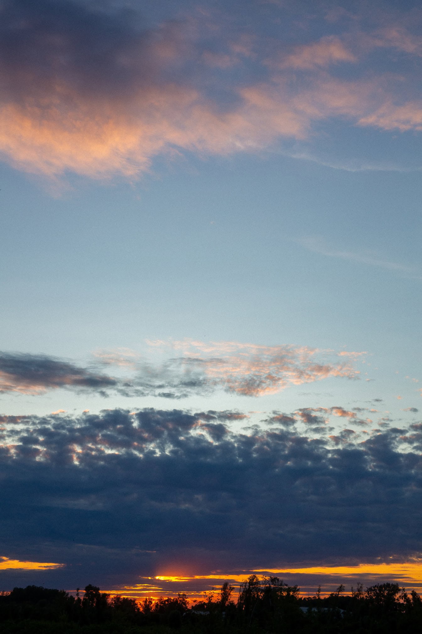 Sininen taivas tummilla pilvillä ja oranssilla auringonsäteellä hämärässä