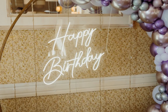 A Happy Birthday sign, a glowing white neon sign hanging from a balloon arch