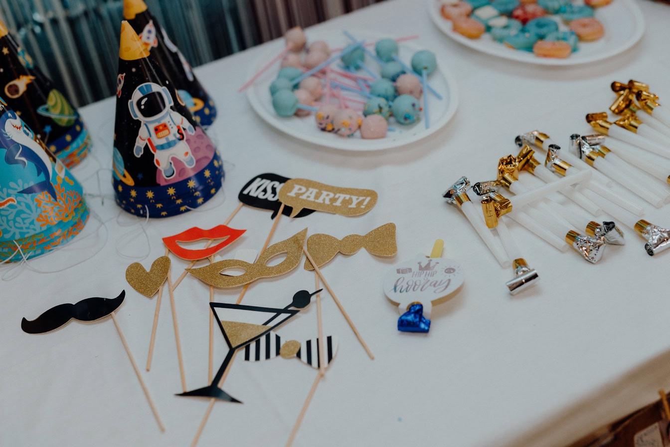 Mesa con piruletas en el plato y accesorios de cumpleaños del bebé, como gorros de cumpleaños, máscaras y sopladores