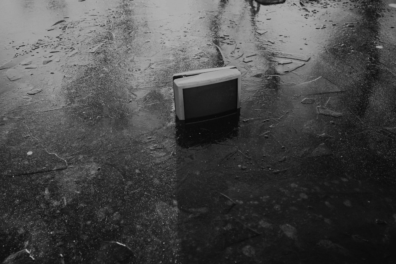 Un estanque congelado con un viejo televisor desechado, una foto en blanco y negro de la contaminación de las vías fluviales