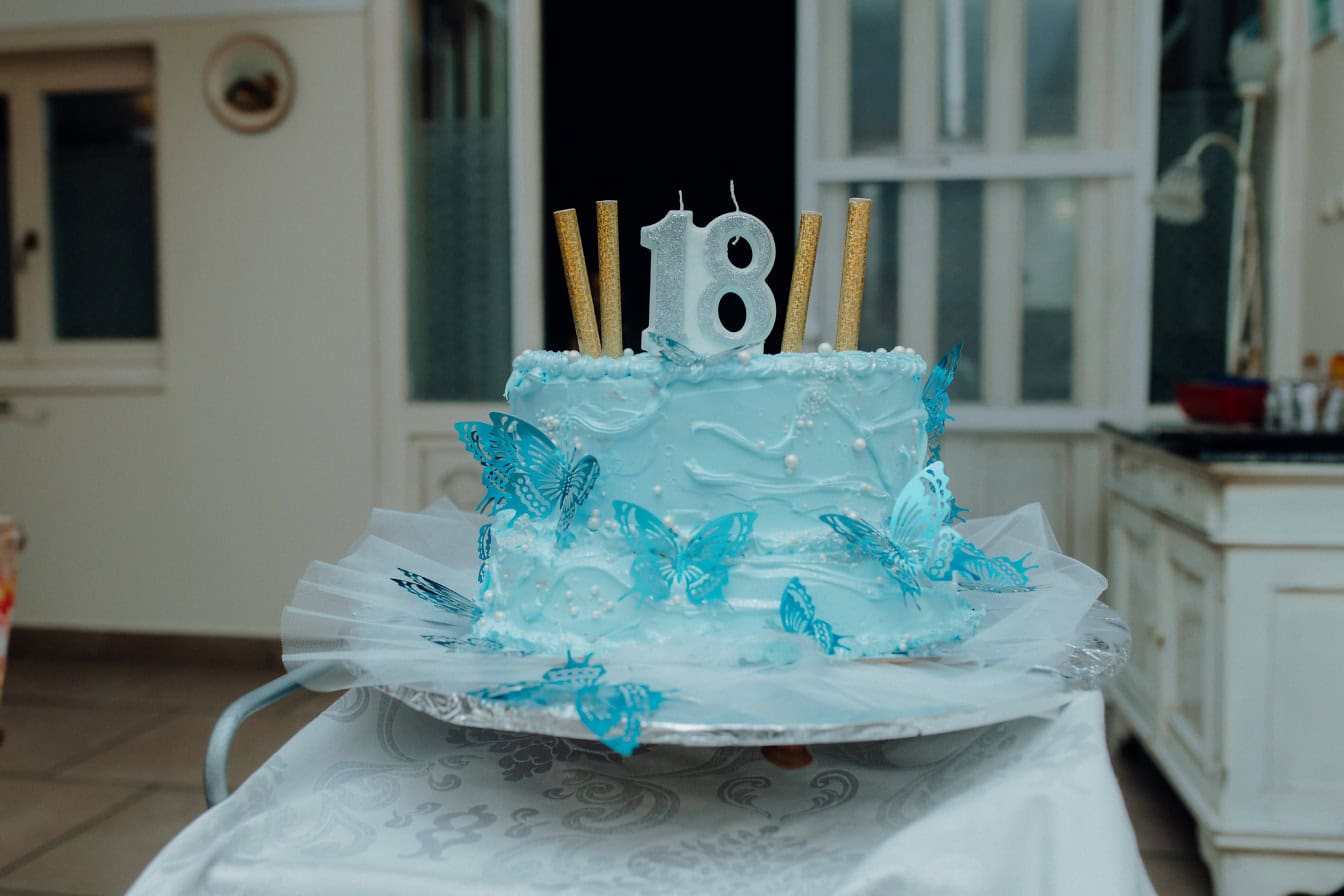 Torta di compleanno blu con candelina a forma di numero diciotto (18) e con farfalle e glassa sopra